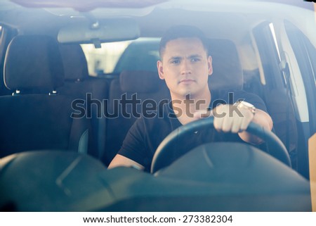 Portrait of a good-looking young man driving his car, shot through the windshield