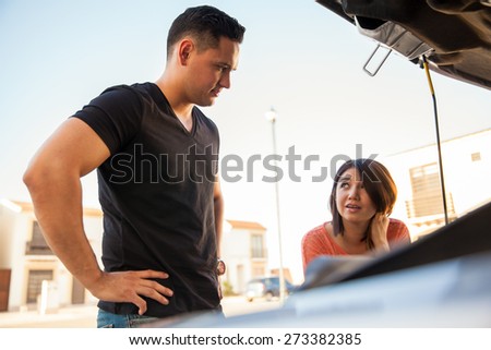 Young couple looking at a car with the hood open trying to fix it