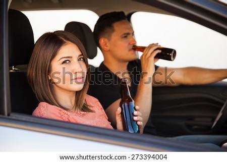 Portrait of a young Hispanic woman and her date drinking beer while driving a car