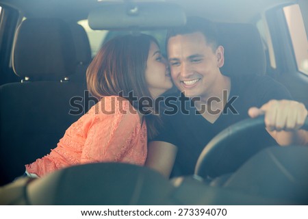 Beautiful young woman kissing her boyfriend in the cheek while he drives. Shot through the windshield