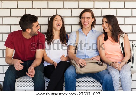 Group of Latin college friends talking and having some fun while sitting in a bench in the school hallway
