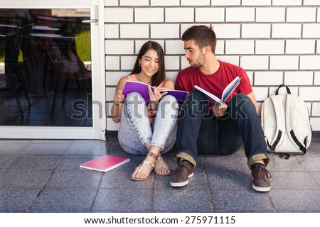 Couple of college students sitting outside a classroom and studying together