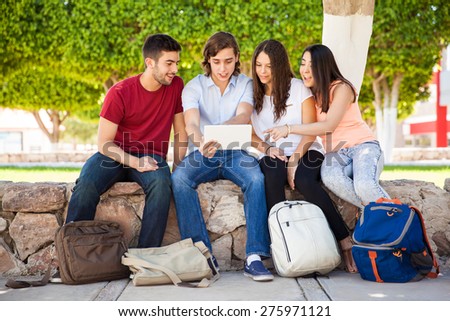 Group of Latin college students looking at something online on a tablet computer at school