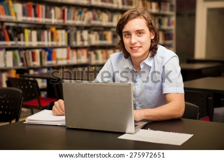 Attractive young man using a laptop for homework in the school library
