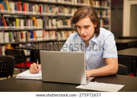 Attractive male college student using a laptop and doing some homework in the school library