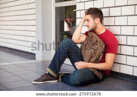 College student sitting outside a classroom with a hand on his hair, feeling stressed and upset about his grades