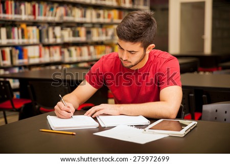 Good looking young man taking some notes and doing school work in a library