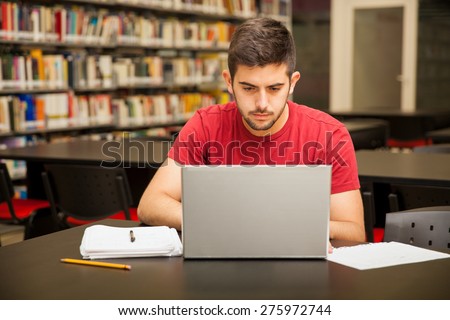 Handsome young college student using a laptop for school work in the library