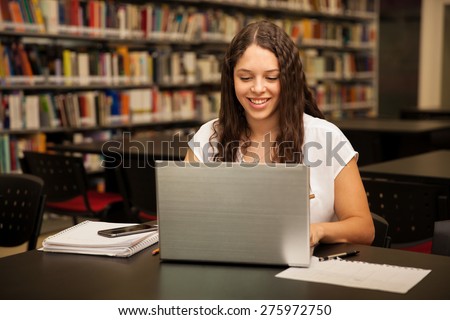 Cute female college student using a laptop and doing some homework in the school library
