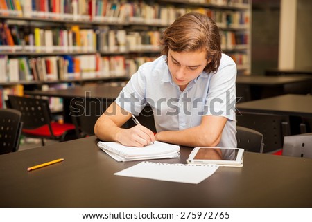 Young caucasian man taking some notes and doing homework in the school library