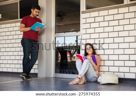 Couple of university students waiting in the hallway outside a classroom and studying