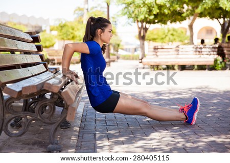 Profile view of a female athlete doing some tricep dips on a park bench