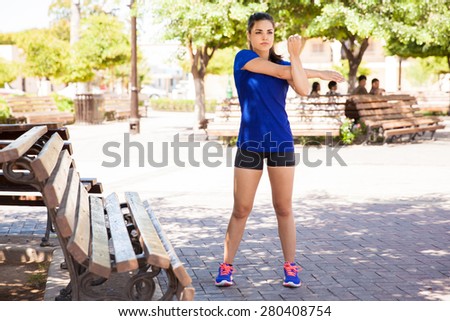 Full length portrait of a young female runner stretching and warming up outdoors next to a park bench