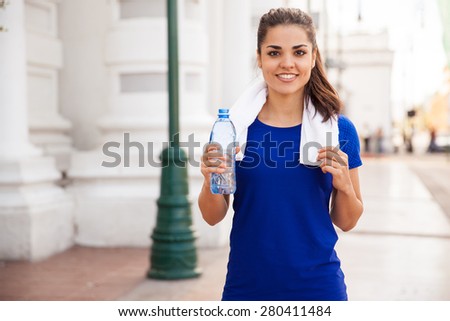 Portrait of a beautiful Latin woman relaxing and drinking water after jogging in the city