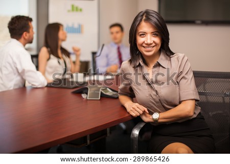 Beautiful Hispanic young lawyer sitting in a meeting room with some of her colleagues and smiling
