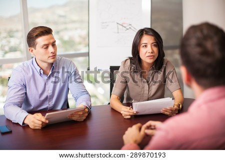 Couple of Latin people with resume in hand, interviewing a job candidate in a meeting room