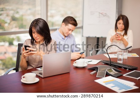 Hispanic people in a meeting room ignoring their work and doing some social networking on their smartphones