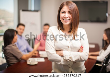 Beautiful young woman standing in a meeting room with a group of people working in the background