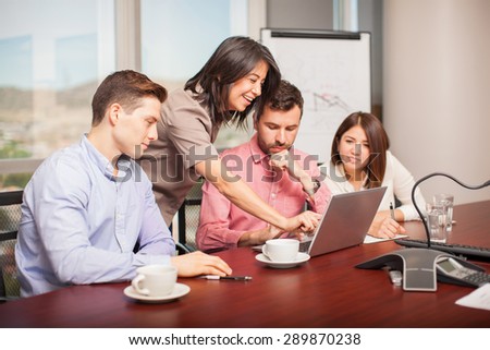 Four Latin young people dressed casually looking at a laptop computer and working in a meeting room