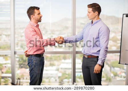 Nervous young man giving a handshake to his confident and intimidating boss in his office