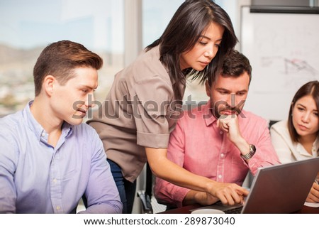 Pretty young Hispanic woman reviewing the work of her co-workers and giving them advice