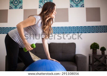 Attractive pregnant brunette exercising with dumbbells and a stability ball at home