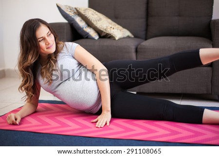 Good-looking pregnant brunette lifting her legs and exercising while lying on the floor at home