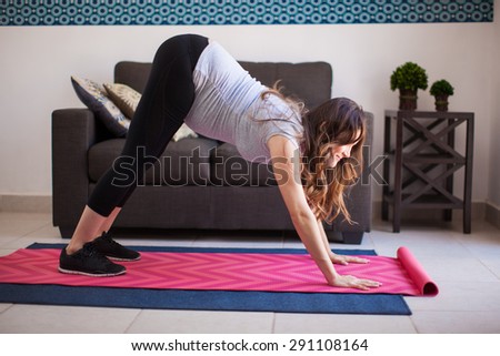 Profile view of a young pregnant woman trying the downward dog yoga pose at home