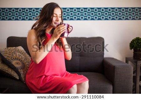 Happy pregnant mother smelling a cup of hot tea in the morning at home