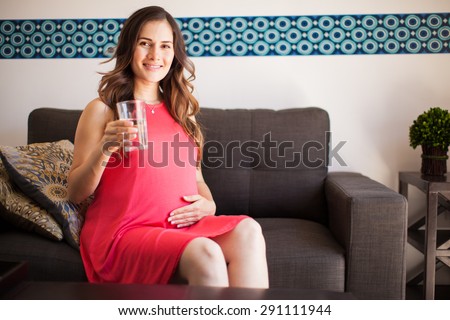 Cute young pregnant mom drinking water from a glass while relaxing at home