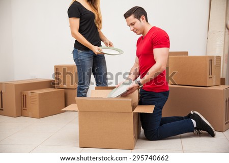 Young man and his girlfriend putting some of their stuff in boxes before moving out to their new place