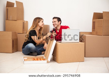 Happy young couple taking a break from unpacking boxes and watching a show in a laptop while eating pizza