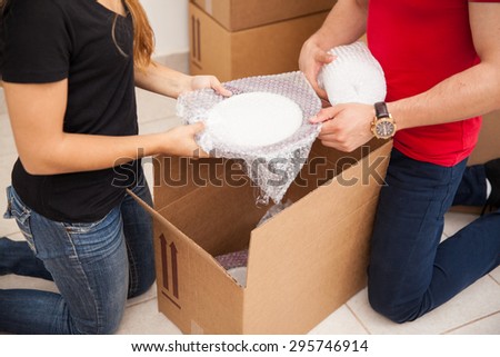 Closeup of a young couple using bubble wrap to pack their stuff in boxes before moving out