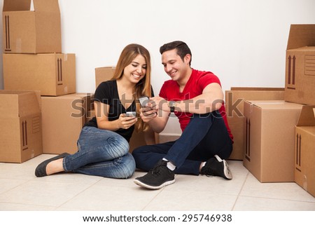 Happy young couple taking a break from unpacking and sharing photos with their smartphones