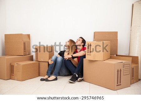 Cute young couple sitting in the floor of their new home while unpacking and looking towards copy space