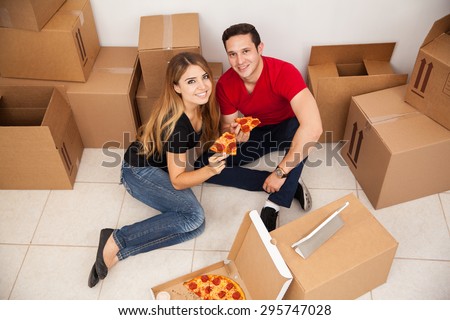 High angle view of a young couple unpacking boxes in a new home and eating some pizza together