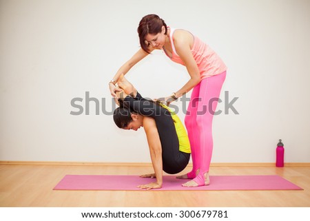 Female yoga instructor helping a woman with a pose in a yoga studio