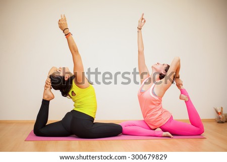Pretty female friends holding the pigeon pose together in a yoga studio