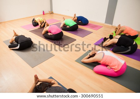 Wide view of a large group of young women stretching and meditating during a yoga class