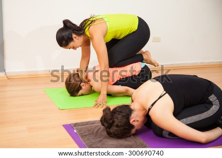 Young female yoga instructor pushing a student for a correct pose during class