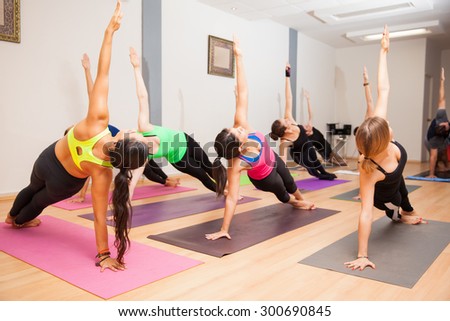 Young female yoga instructor doing a side plank with the rest of her class
