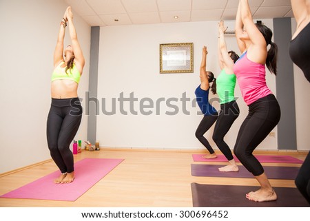 Pretty young yoga instructor and a group of students doing the chair pose during a yoga class