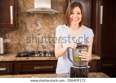 Beautiful young brunette making some green juice in a blender at home and smiling
