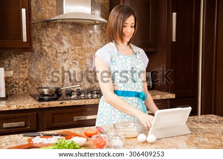 Beautiful young woman reading a recipe on a tablet computer while cooking dinner in the kitchen