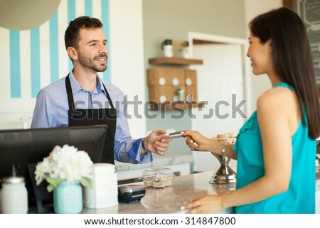 Young brunette paying with a credit card at the cash register in a cake shop