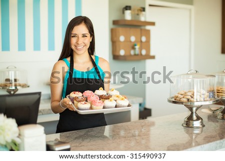 Portrait of a beautiful female business owner showing some of her freshly baked cupcakes and smiling