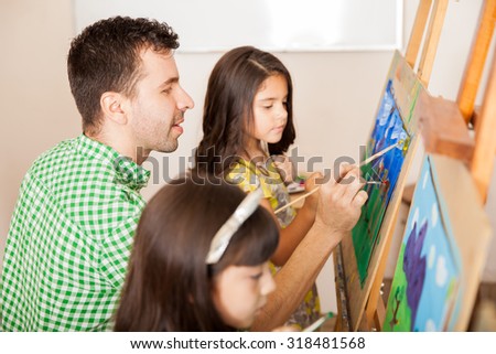 Profile view of a handsome art teacher working on a painting with one of his students in class