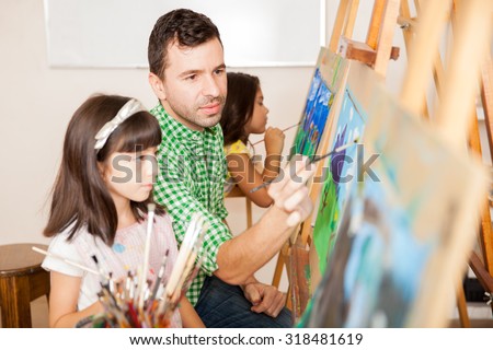 Portrait of an attractive Hispanic art teacher helping a little girl with her painting
