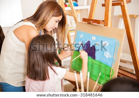 Cute art class teacher and a little girl painting together a landscape at school