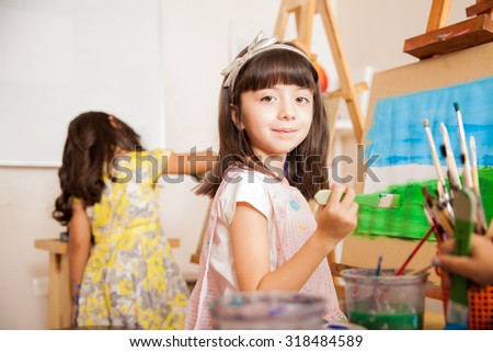 Portrait of a pretty little artist holding a brush and smiling while working on a painting for art class
